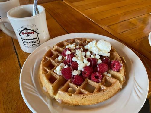 A plate of waffles topped with raspberries and white chocolate chips, served with a coffee mug in the background.