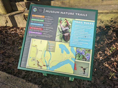 Sign displaying a map and trail rules for museum nature trails, featuring various trail names and distances.