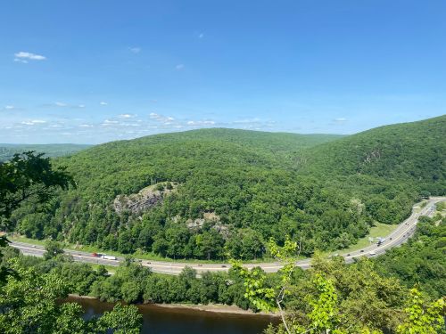 A scenic view of lush green hills, a winding river, and a highway under a clear blue sky.