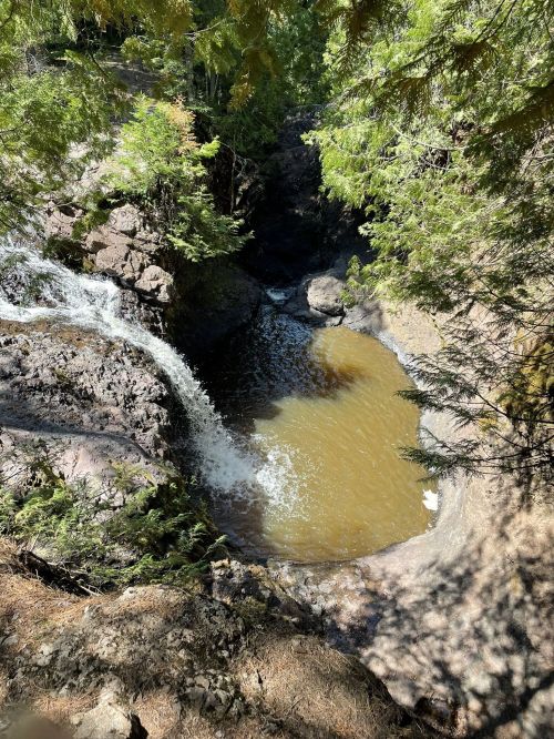A serene waterfall cascading into a calm pool, surrounded by lush greenery and rocky terrain.