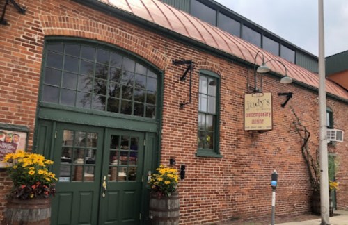 Exterior of a brick restaurant with a green door, sign reading "Judy's Contemporary Cuisine," and flower planters.
