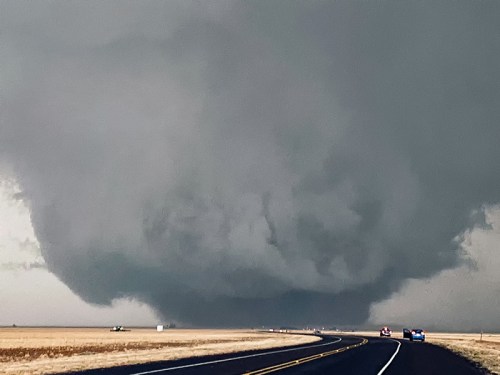 A dark, ominous cloud looms over a deserted road, hinting at severe weather conditions ahead.