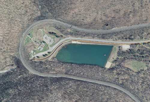 Aerial view of a winding road near a green lake surrounded by trees and a small building.