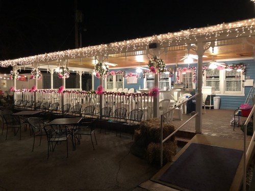 A cozy outdoor dining area decorated with pink accents and string lights, creating a festive nighttime atmosphere.