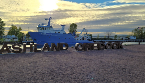 A blue boat docked near a sign reading "Ashland Oredock" under a cloudy sky.