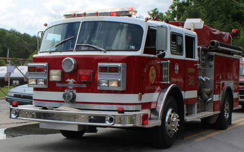 A red fire truck with emergency lights parked on a street, featuring a shiny chrome front and various firefighting equipment.