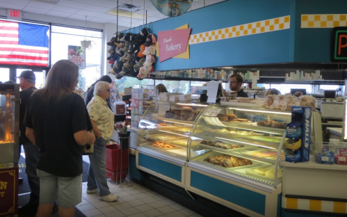 A busy bakery with a display case of pastries, customers in line, and an employee serving at the counter.
