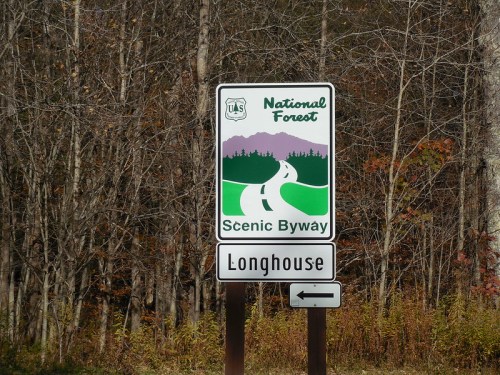 Sign for a National Forest Scenic Byway, featuring a winding road and the word "Longhouse" with a left arrow.