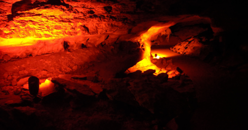 A dimly lit cave with orange lighting illuminating rocky paths and formations.