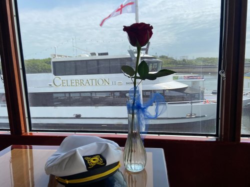 A rose in a vase and a captain's hat on a table, with a boat named "Celebration II" visible through the window.