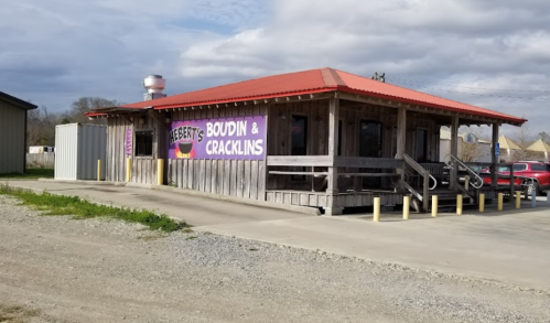 A rustic building with a red roof and wooden exterior, featuring a sign for "Reesey's Boudin & Cracklins."