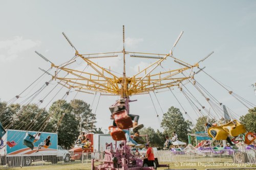 A colorful swing ride at a fair, with people enjoying the ride against a clear blue sky and trees in the background.