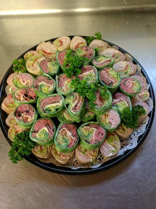 A circular platter filled with colorful rolled sandwiches, garnished with parsley and arranged neatly.