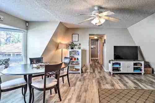 Cozy living space featuring a dining table, ceiling fan, TV, and light-colored walls with wooden flooring.