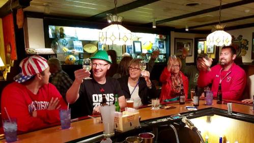 A group of friends at a bar raising glasses in a toast, wearing festive hats and enjoying drinks together.