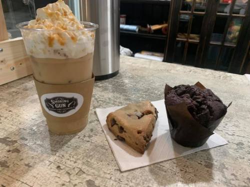 A delicious iced coffee topped with whipped cream and caramel, alongside a chocolate muffin and a cookie on a plate.