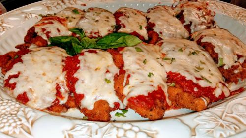 A platter of breaded chicken topped with marinara sauce and melted cheese, garnished with fresh basil.