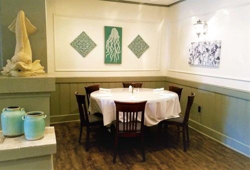 A cozy restaurant corner with a round table, wooden chairs, and decorative wall art featuring jellyfish and abstract designs.