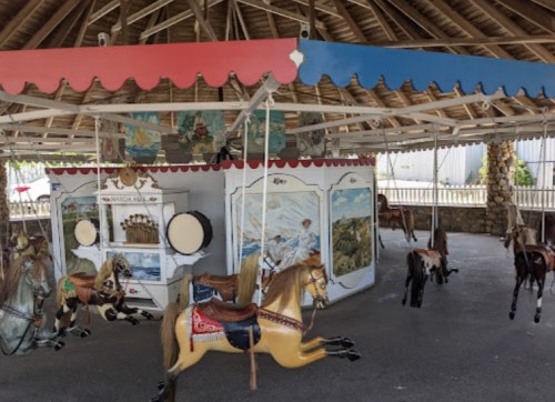 A vintage carousel with wooden horses, colorful canopies, and a scenic backdrop, set in a covered area.