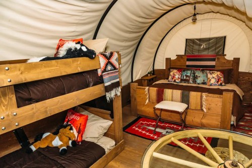 Cozy interior of a glamping tent featuring a bunk bed, a double bed, and rustic decor with plush toys.