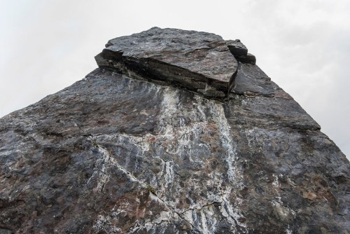 A close-up view of a large, rugged rock formation against a cloudy sky.