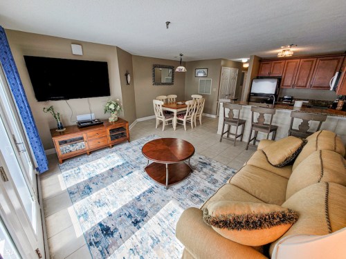 Bright living area with a sofa, coffee table, TV, dining table, and kitchen in a modern, open layout.