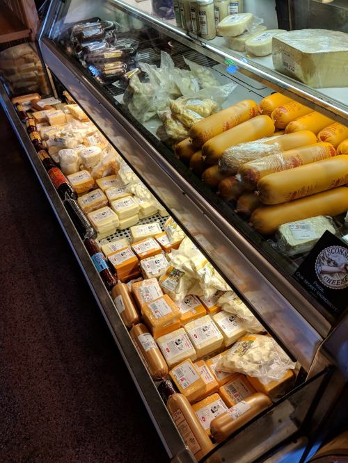 A display case filled with various cheeses and butternut squash, showcasing a variety of shapes and packaging.