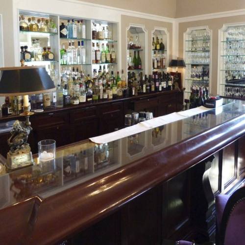 A polished bar with a variety of liquor bottles displayed on shelves behind it, and a glass countertop reflecting the light.