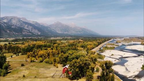 A scenic view of mountains, a river, and a red barn surrounded by trees in a lush landscape.