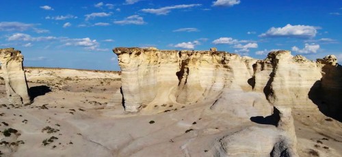 A vast desert landscape featuring unique rock formations under a blue sky with scattered clouds.