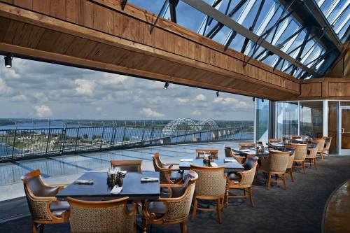 A modern dining area with wooden accents, large windows, and a view of a river and bridge under a cloudy sky.