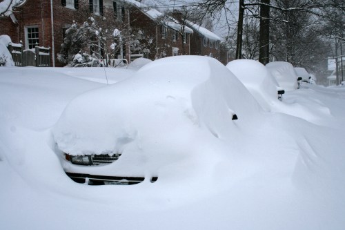 Cars buried under deep snow in a residential area during a winter storm.