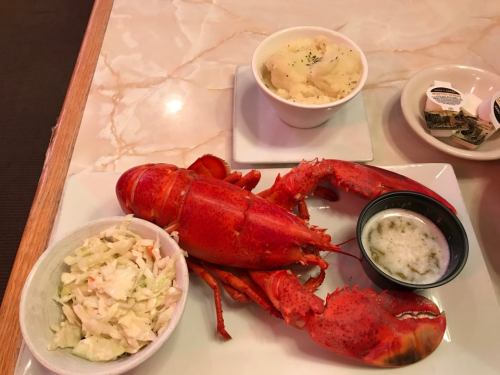 A whole cooked lobster served with coleslaw and a side of mashed potatoes on a table.