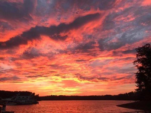 Vibrant sunset over a lake, with dramatic red and orange clouds reflecting on the water's surface.