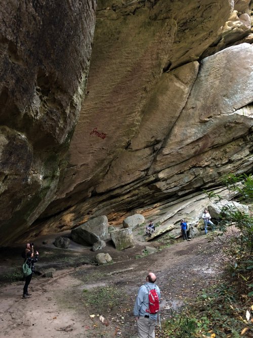A group of people exploring a rocky cave with large boulders and a steep overhang above them.