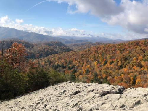 A scenic view of colorful autumn foliage covering rolling hills under a partly cloudy sky.