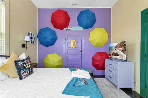 Colorful room featuring a bed, a TV, and vibrant umbrellas on the wall, creating a cheerful atmosphere.