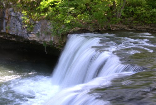 A serene waterfall cascading over rocky cliffs, surrounded by lush green foliage and flowing into a calm river.