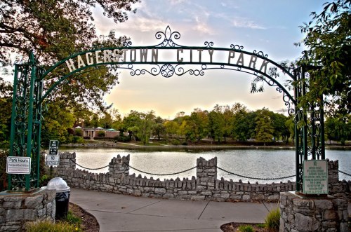 Entrance to Hagerstown City Park, featuring a decorative archway and a serene lake surrounded by trees.