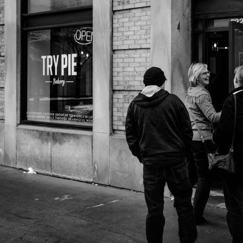 A group of people outside a bakery called "Try Pie," with an open sign in the window. Black and white photo.
