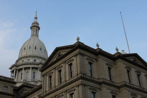 The image shows the dome of a historic government building against a blue sky.