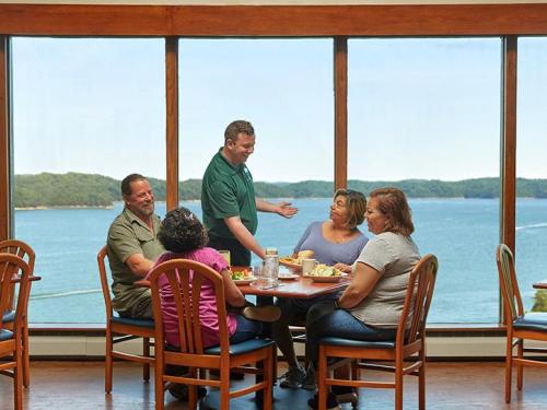 A group of five people dining at a table with a scenic view of water and hills in the background.