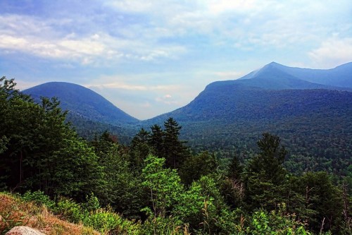 A scenic view of two mountains surrounded by lush green forests under a cloudy sky.