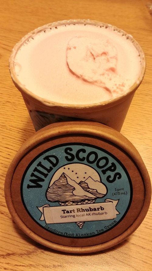 A pint of Wild Scoops ice cream with a pink tart rhubarb flavor, featuring a wooden lid and a scenic label design.