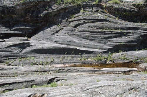 Layered rock formations with green vegetation and a small stream running through the crevices.