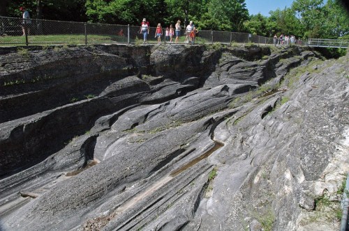 A rocky landscape with layered stone formations and a group of people walking along a fence in the background.