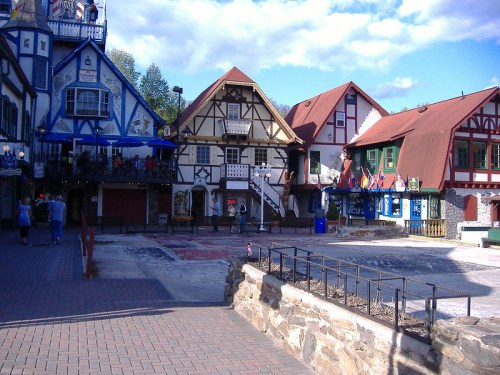 Colorful, Bavarian-style buildings line a cobblestone street, with people walking and a clear blue sky above.