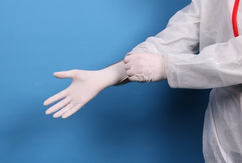 A person in a protective suit putting on a white latex glove against a blue background.