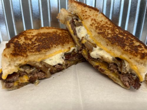 A grilled sandwich cut in half, featuring layers of beef, melted cheese, and onions on toasted bread.