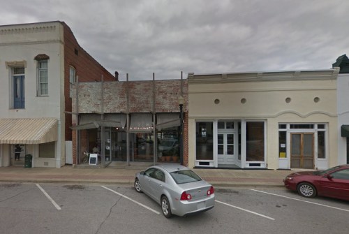 A street view of two adjacent buildings with a gray car parked in front, under a cloudy sky.